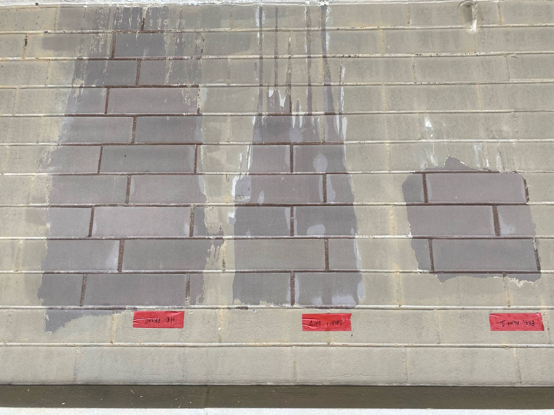 Three rectangular patches of wet pavement, each labeled with a small red tag, are visible on a dry brick surface.