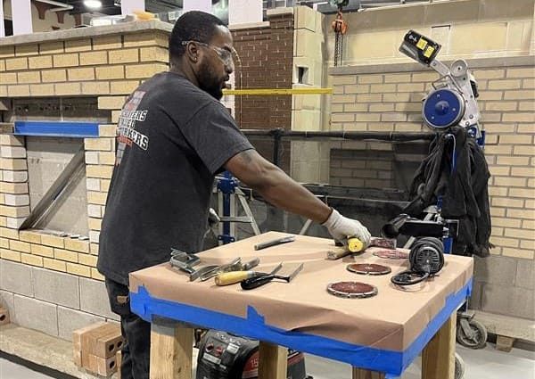 A man is measuring something on a table in a workshop.