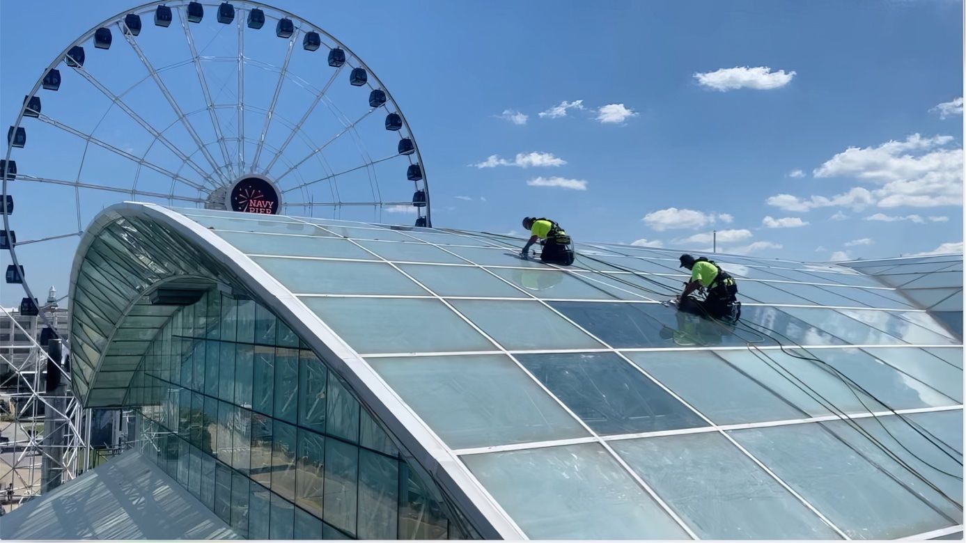 Two men are working on the roof of he crystal garden with a ferris wheel in the background.