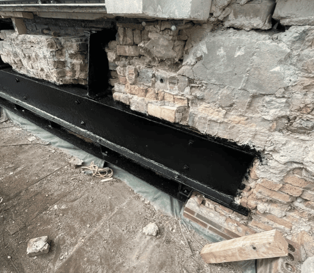 Damaged concrete wall with a long black trench opening at the base, debris and broken bricks nearby