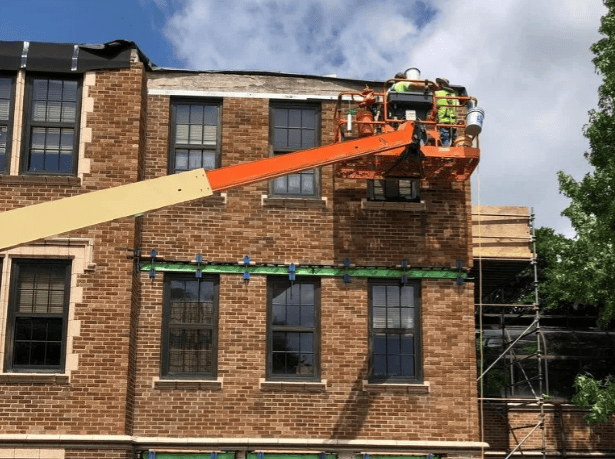 Two workers in an orange lift repairing a brick building’s roofline