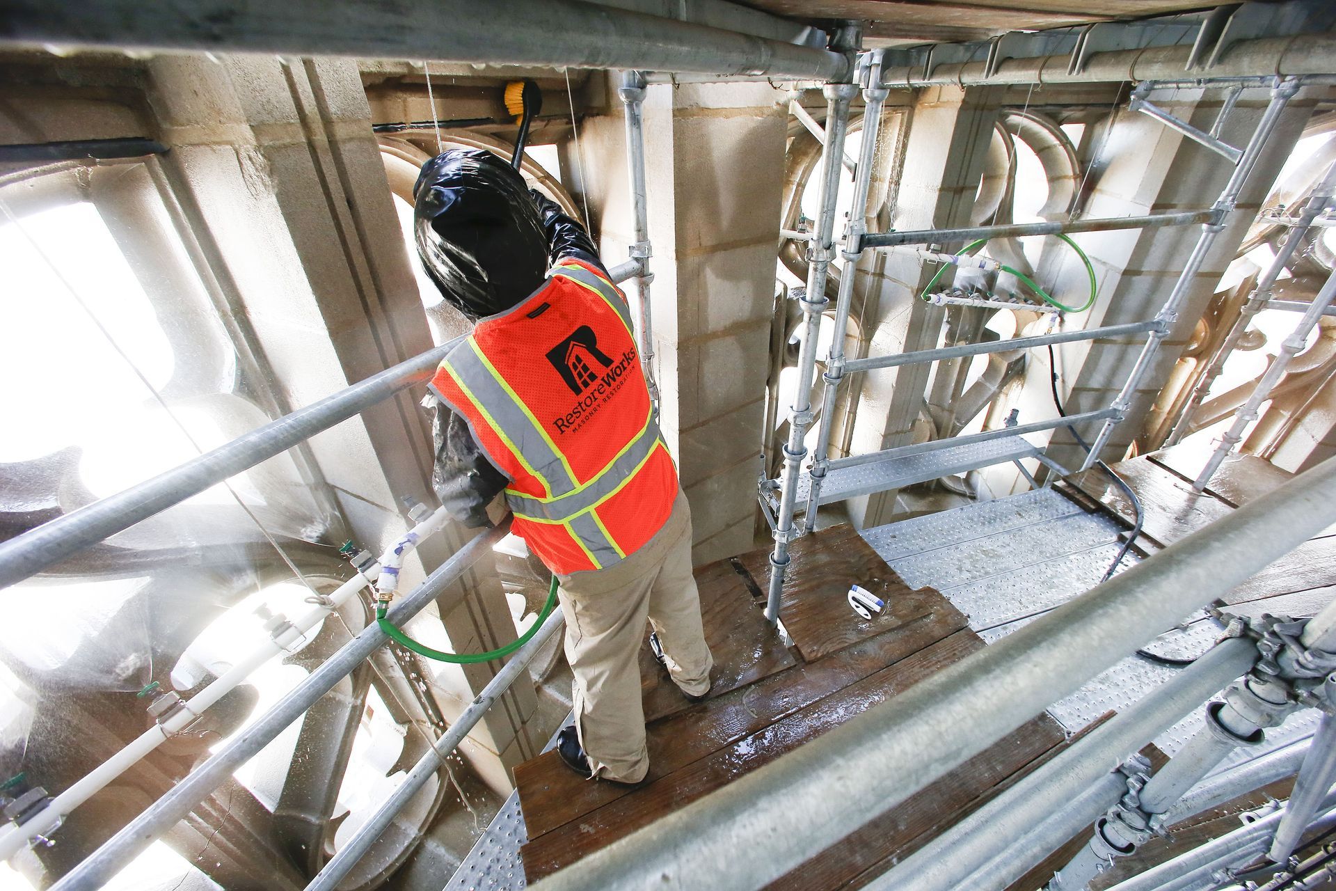 A construction worker in a high-visibility vest works on scaffolding near the carved stone details of a building.