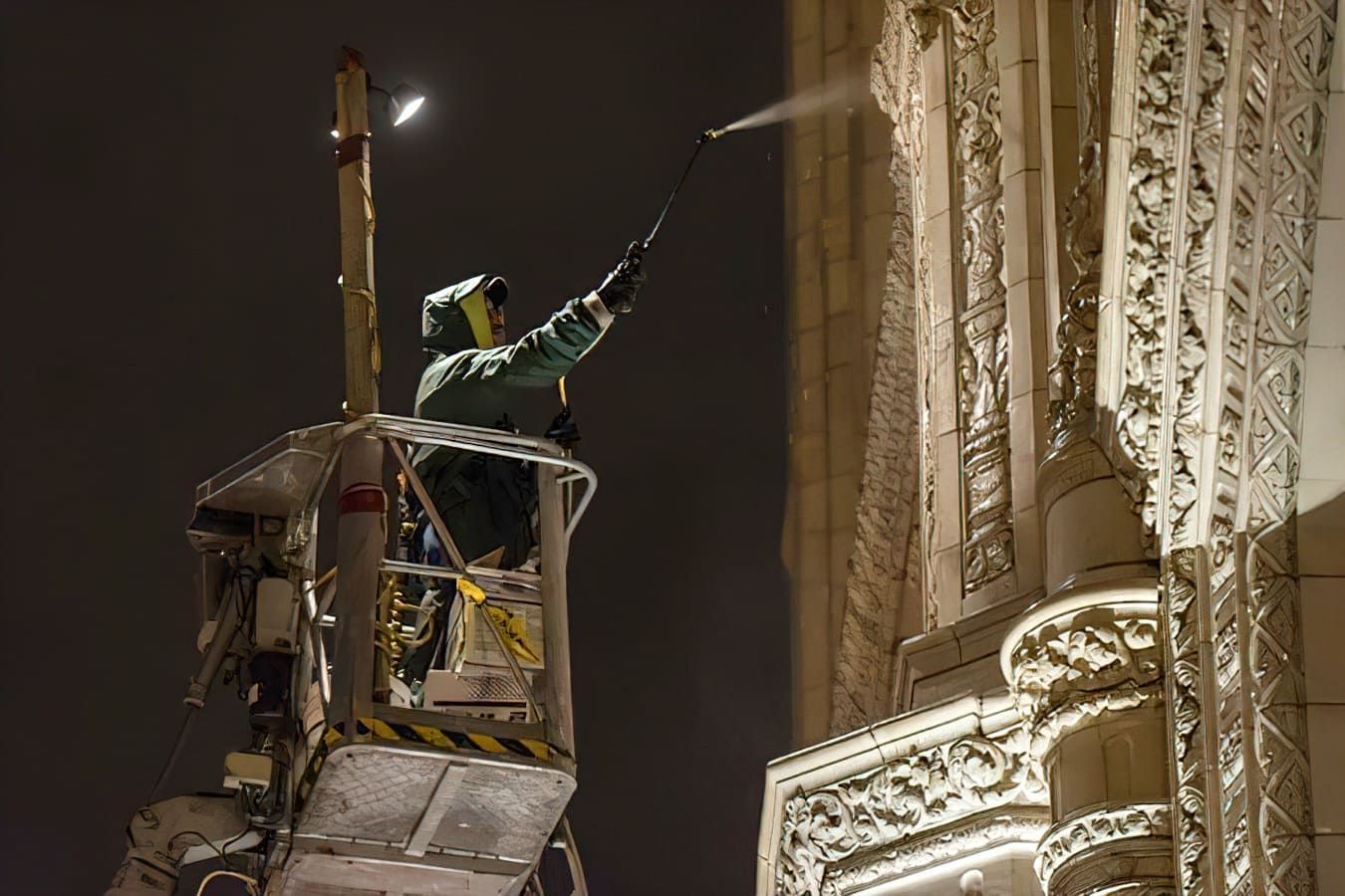 Worker on a lift spray-cleaning a tall ornate building at night