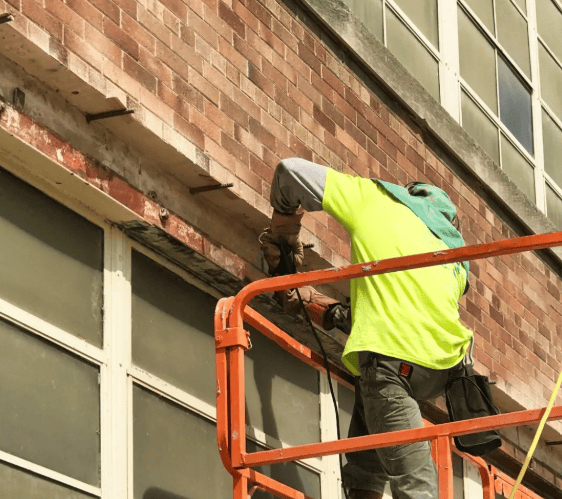 Worker in a neon vest repairs brick wall from an orange lift platform