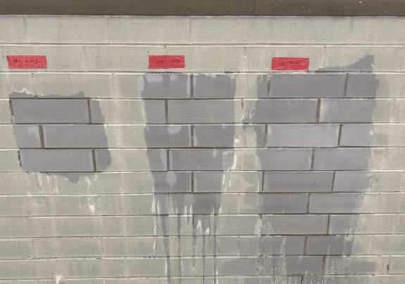 Gray cinder block wall with three wet patches and red labels above each section