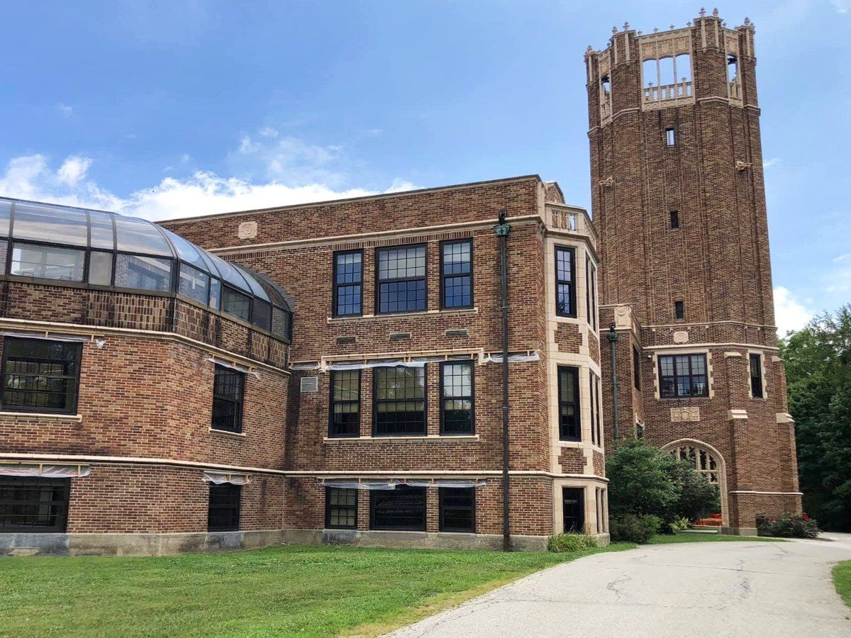 Brick building with tower, blue sky, and a curved glass roof section. A driveway leads to an arched entrance.