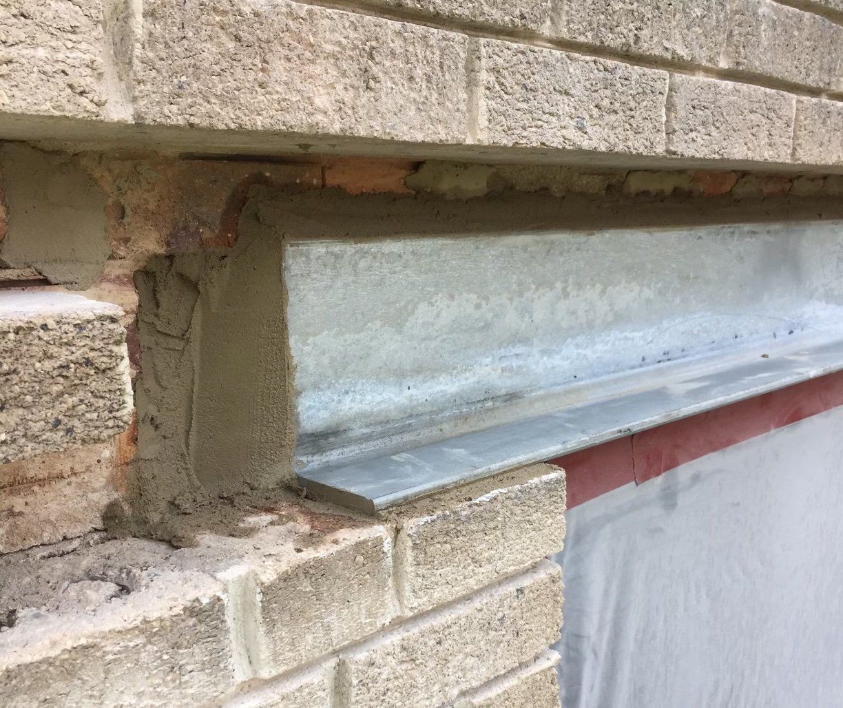 Close-up of brick wall with a metal beam and sealant in a construction setting.