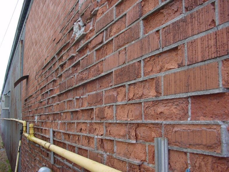 Advanced brick spalling on a masonry wall caused by trapped moisture, freeze–thaw damage, and deteriorated mortar joints.
