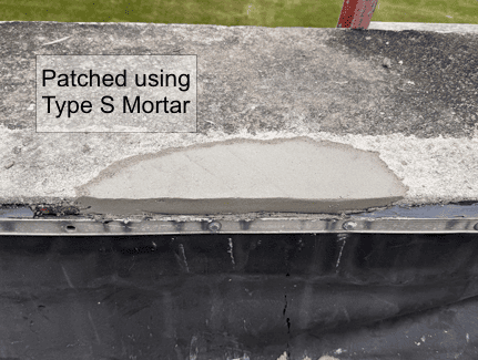 A concrete ledge with a patch of fresh Type S mortar applied over a damaged section above a black roof membrane.