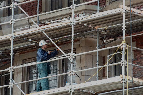 Person in work clothes on scaffolding, cleaning a brick building.