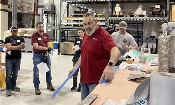 A man in a red shirt is holding a blue tape measure in a warehouse.
