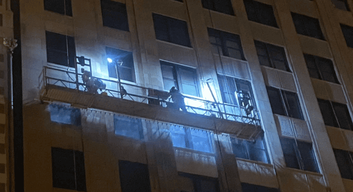 Night view of a building facade with workers on a lit balcony or scaffold during maintenance