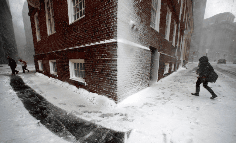 People walk past a snow-covered brick building during a winter storm.