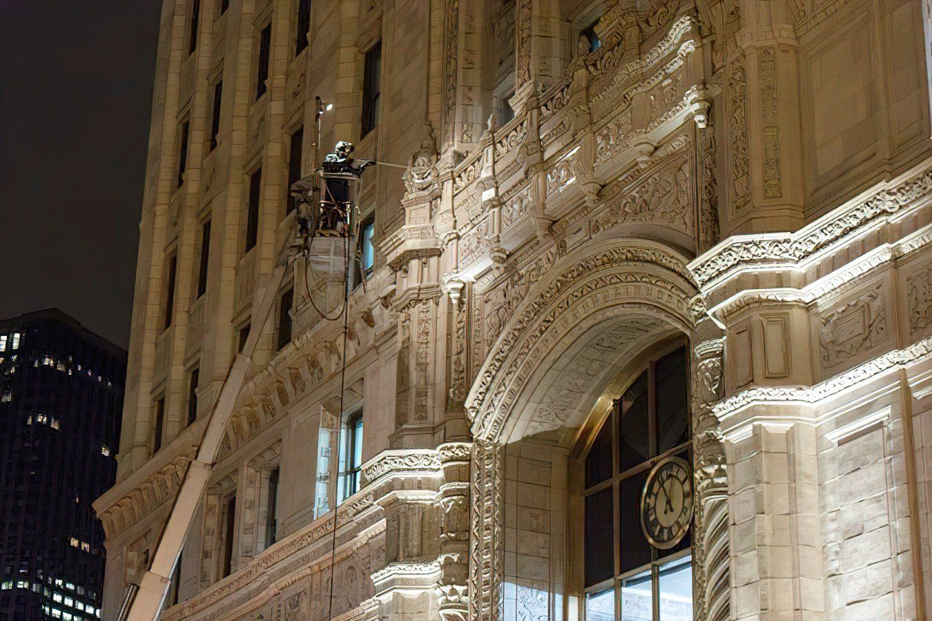 Worker in a lift repairs ornate building facade at night. The building is beige with intricate carvings.