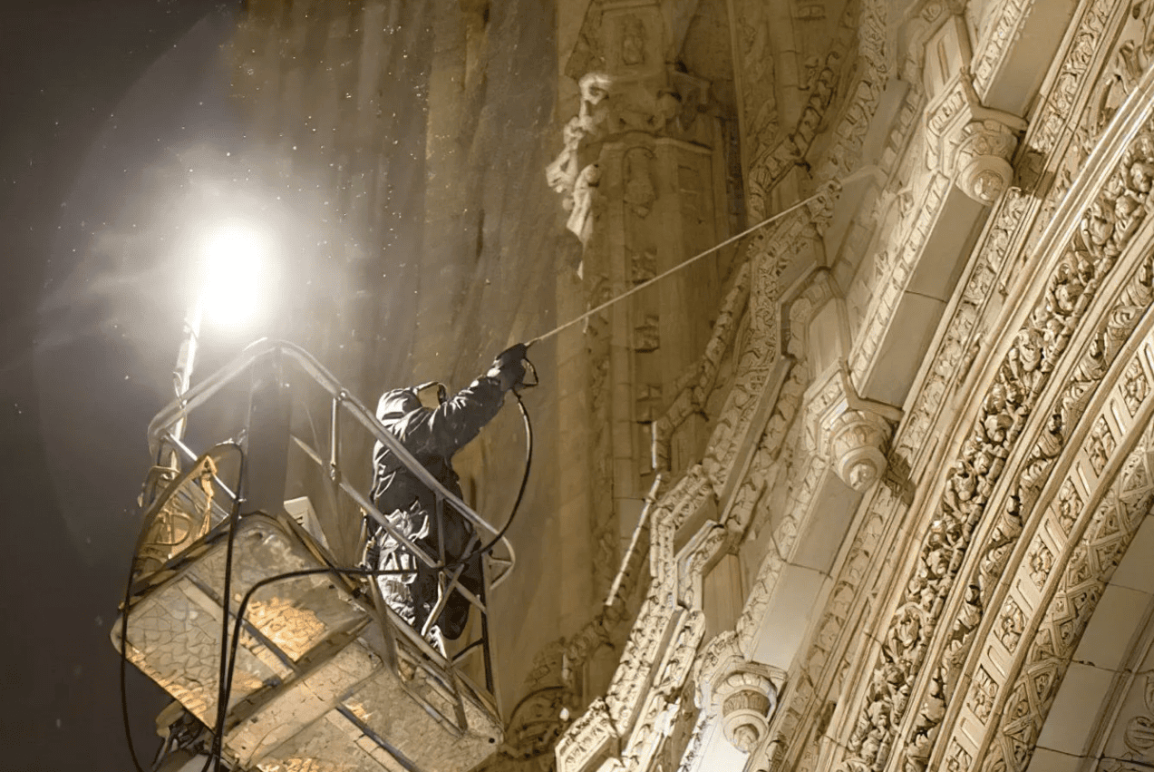 Worker on a lift cleaning ornate cathedral ceiling at night under bright lights