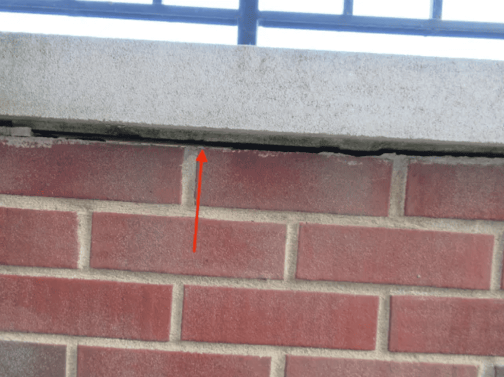Close-up of a brick wall beneath a concrete ledge, with a red arrow pointing to a gap at the top.