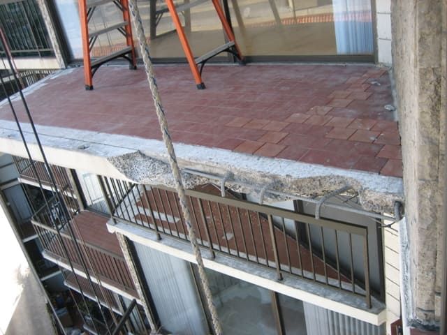 Damaged balcony floor with cracked concrete and exposed railing above a lower walkway