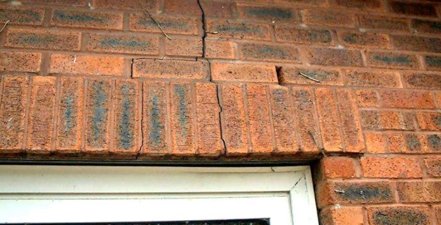 Brick wall above a white window frame with a damaged lintel and missing bricks