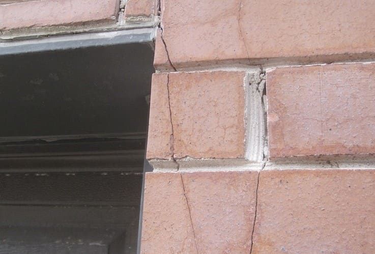 Cracked brick wall beside a black window or doorway frame