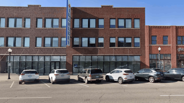 Brick storefront building with large windows and parked cars along the street.