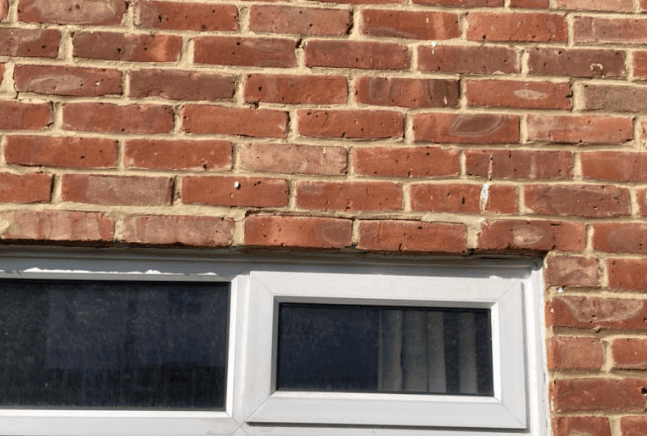 Brick wall above a white-framed window with dark glass panes