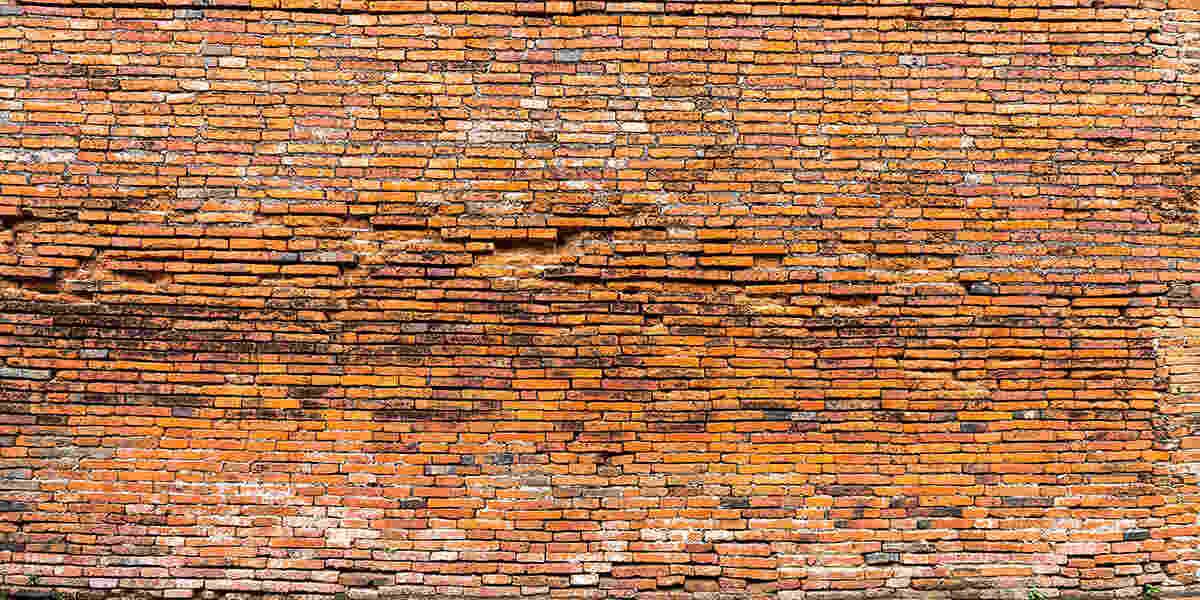 A weathered, horizontal brick wall made of narrow, textured orange-brown bricks with visible mortar and aging.