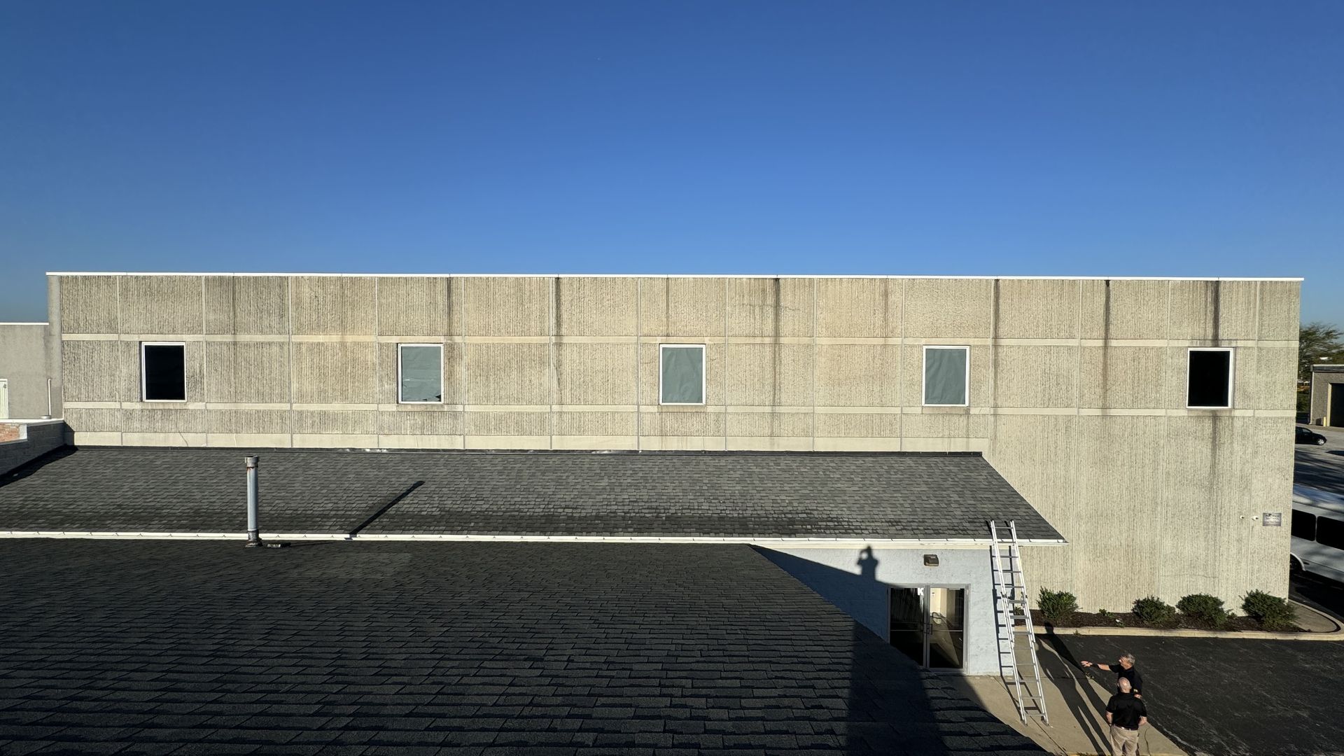 Concrete building facade with small windows, seen across a rooftop under a clear blue sky.