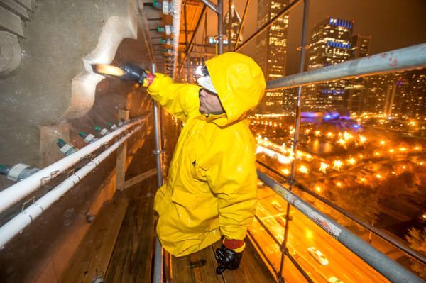 Worker in yellow rain gear inspecting a building facade at night on a city scaffolding platform