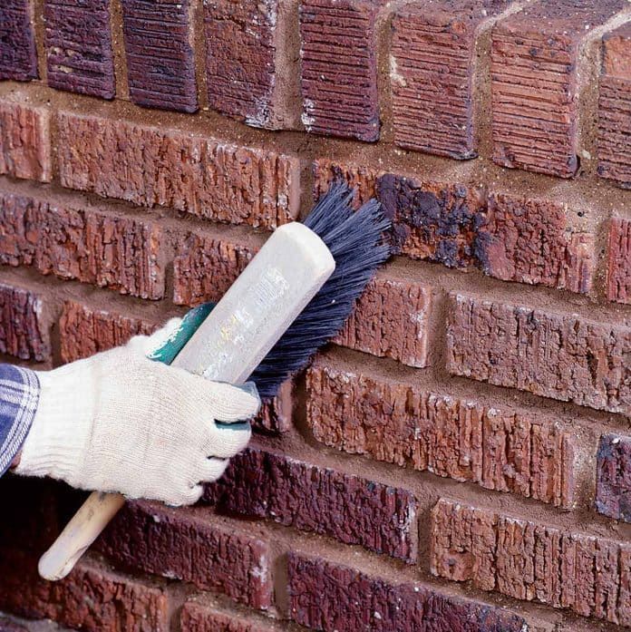 Gloved hands scrubbing a red brick wall with a brush