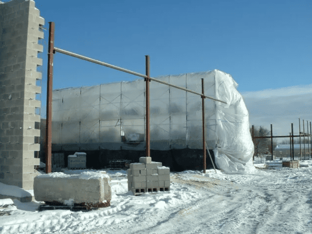 Snow-covered construction site with a large insulated structure and concrete blocks under a clear sky