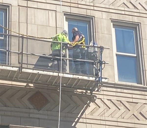 Two workers on a window-washing platform outside a stone building