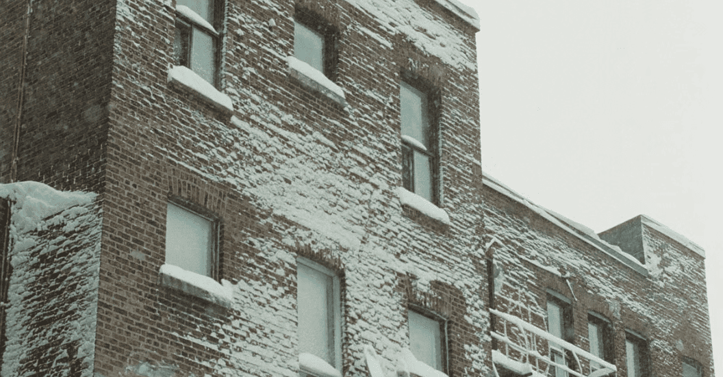 Snow-covered brick apartment building with white-framed windows and snowy rooftop edges