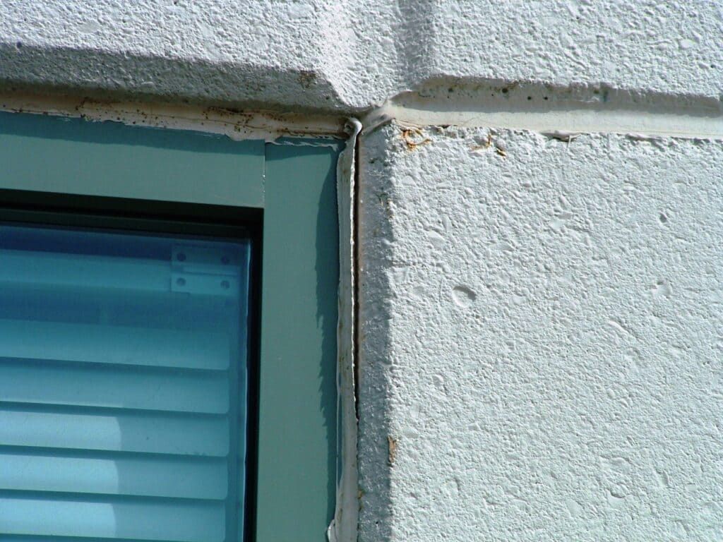 Close-up of a light blue window frame beside a white stucco wall.
