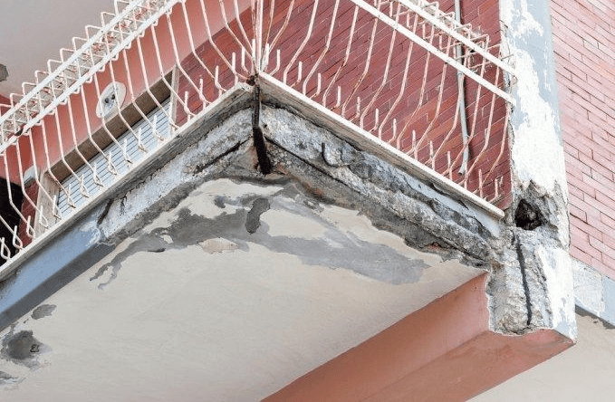 Damaged concrete balcony corner with peeling paint and cracks under a metal railing