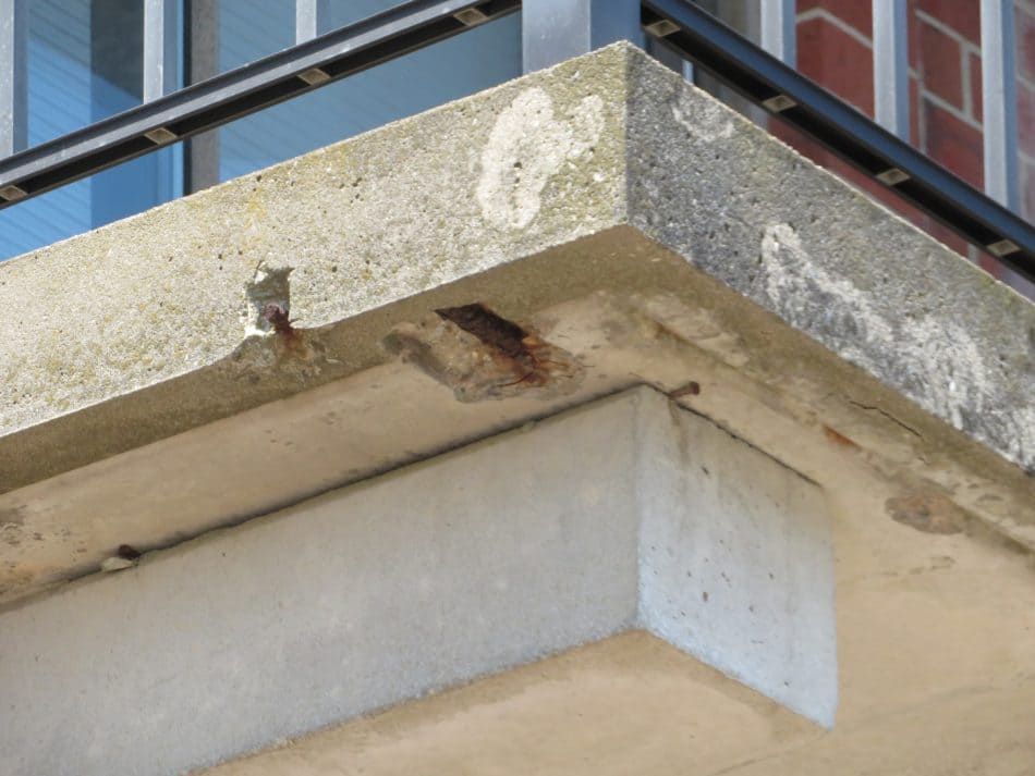Close-up of a concrete building ledge with chipped paint and weathered stains under glass windows