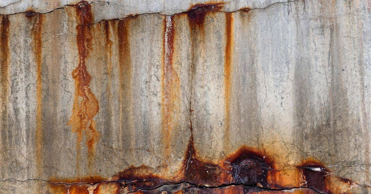 Rust-streaked metal wall with orange corrosion along the bottom edge