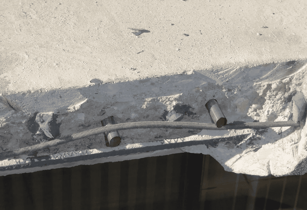 Close-up of a cracked concrete ledge with exposed rebar and a dark opening below