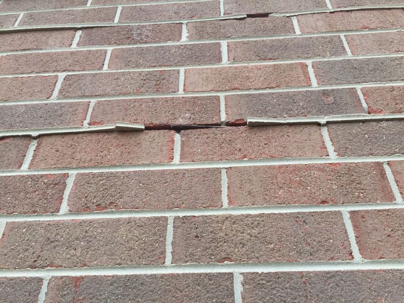 Close-up of a brick wall showing cracked and crumbling mortar joints between the bricks.