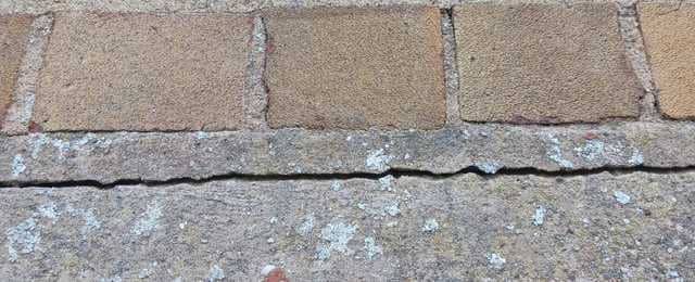 Cracked mortar line between tan brick pavers and a rough concrete edge