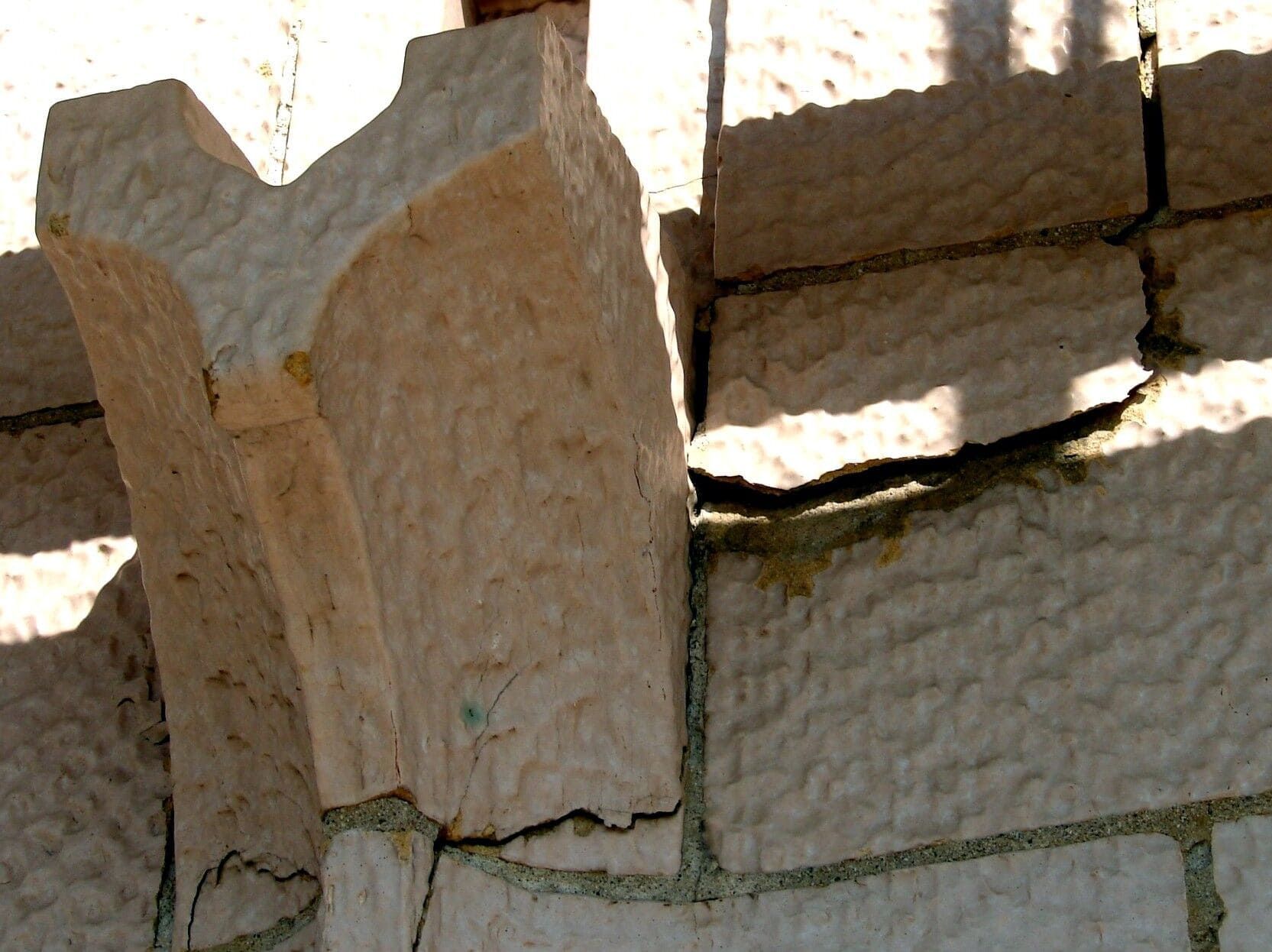 Close-up of weathered stone blocks and a carved pillar in bright sunlight, showing a textured masonry wall.