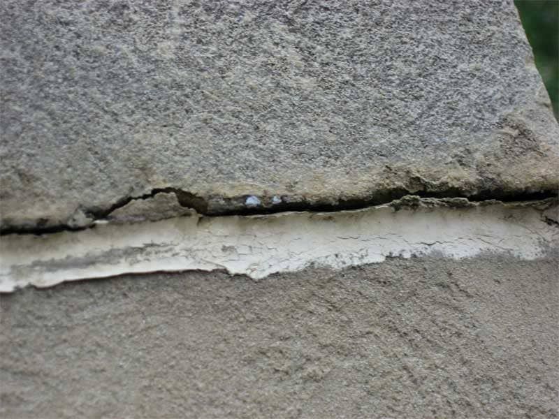 Cracked stone wall with a horizontal gap filled with white mortar