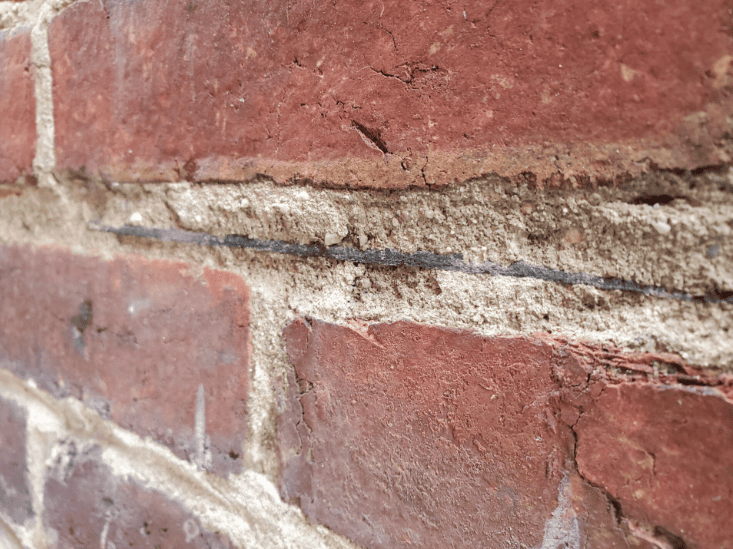 Close-up of a damp red brick wall with cracked mortar and chipped white paint.