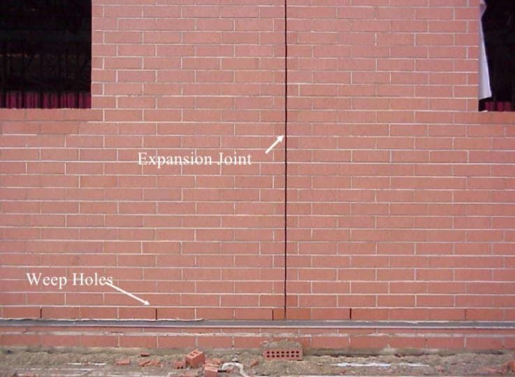 Brick wall with labeled expansion joint and weep holes near the base
