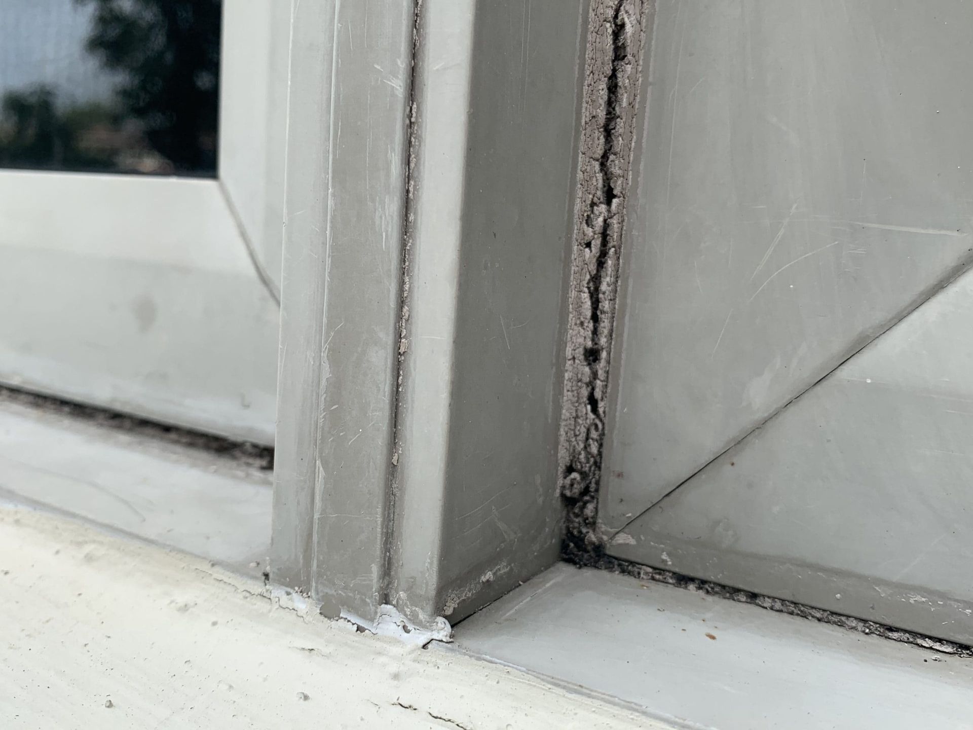 Close-up of a white window corner with visible caulk gaps and peeling sealant.