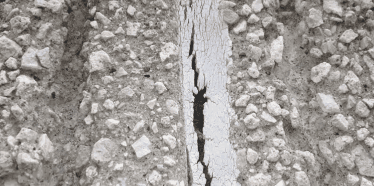 Close-up of cracked concrete with a narrow vertical gap exposing dark space