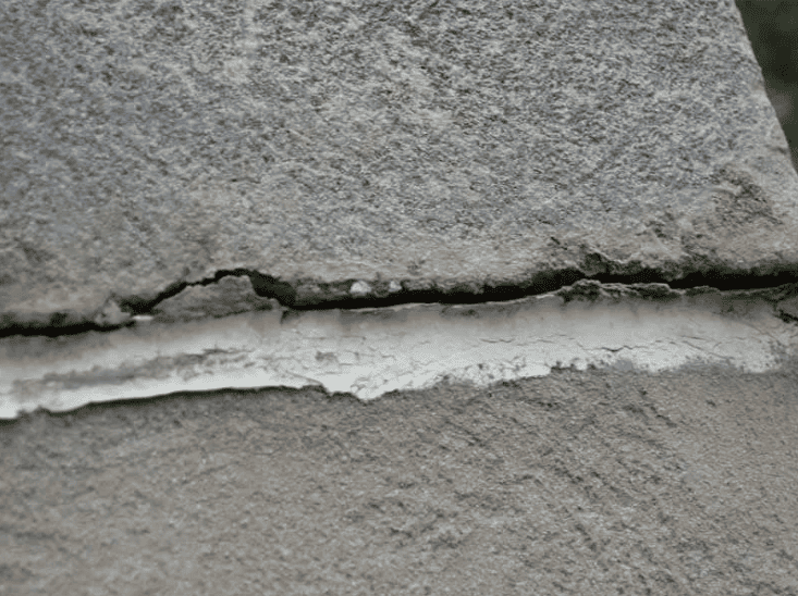 Close-up of a gray stone surface with a horizontal crack filled with white material.