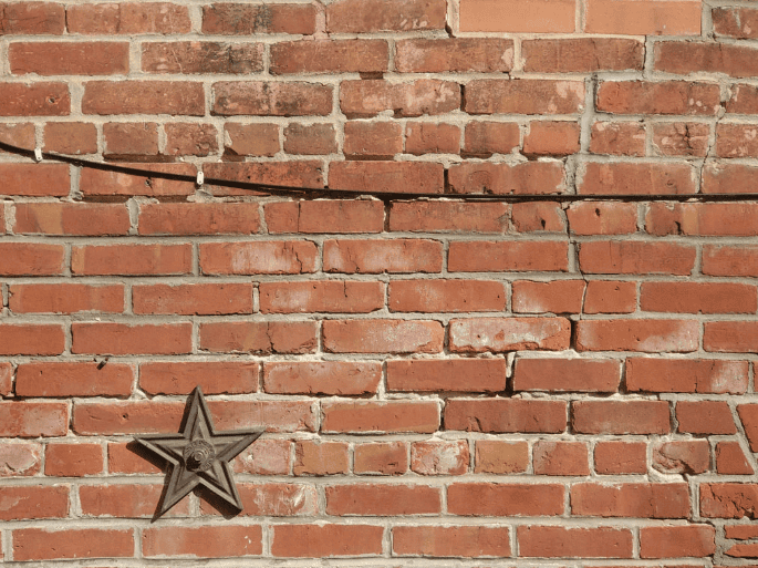 Weathered red brick wall with cracks and a metal star emblem near the lower left