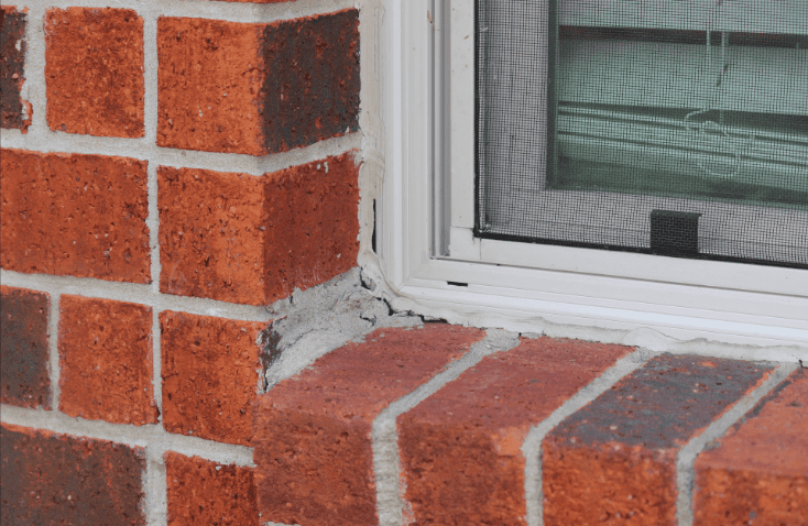 Red brick wall and windowsill with gray mortar repair next to a white-framed window