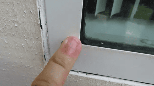 Finger pointing at a small black mark on a white window frame.