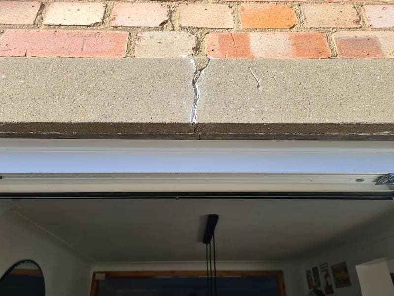 Cracked concrete curb beneath brick pavers above an open garage doorway